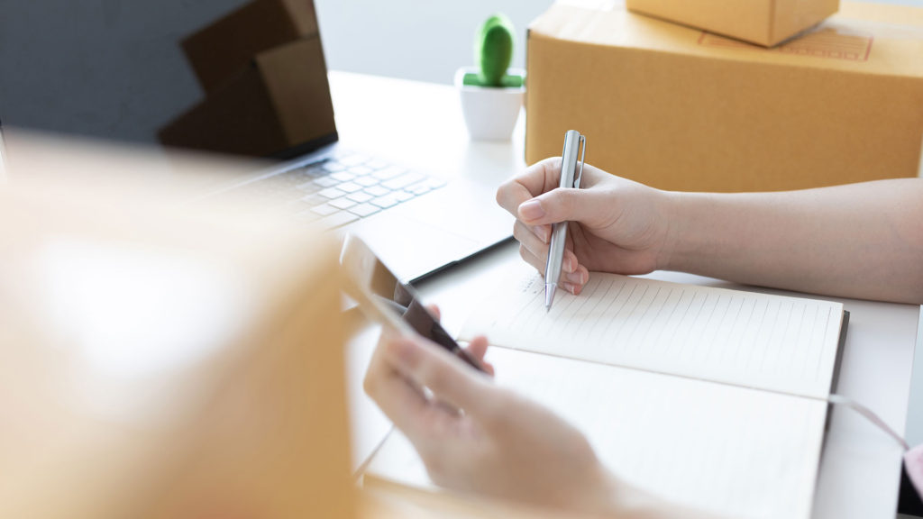 Hands writing on a paper and holding a cel phone