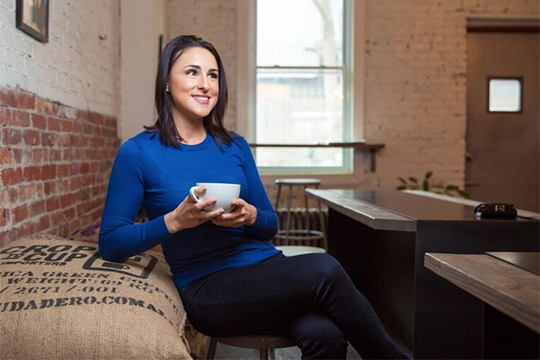 A woman holding a cup of tea with a smile on her face